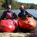 Two kayakers on the water smile for the camera