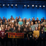 150 people gathered for a group photo with a banner saying "Our time to rise."