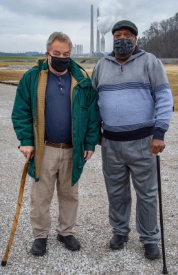 Two men in Covid face masks stand before the power plant 
