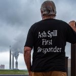 Man with gray hair facing power plant, back of shirt says Ash Spill First Responder