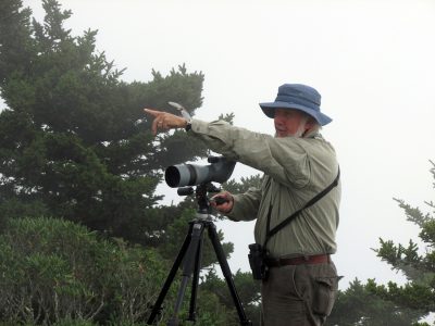 man with spotting scope points toward sky