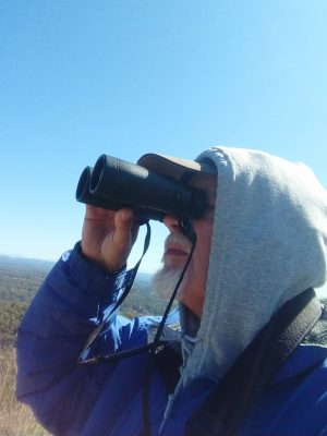 man with gray beard looks at sky with binoculars
