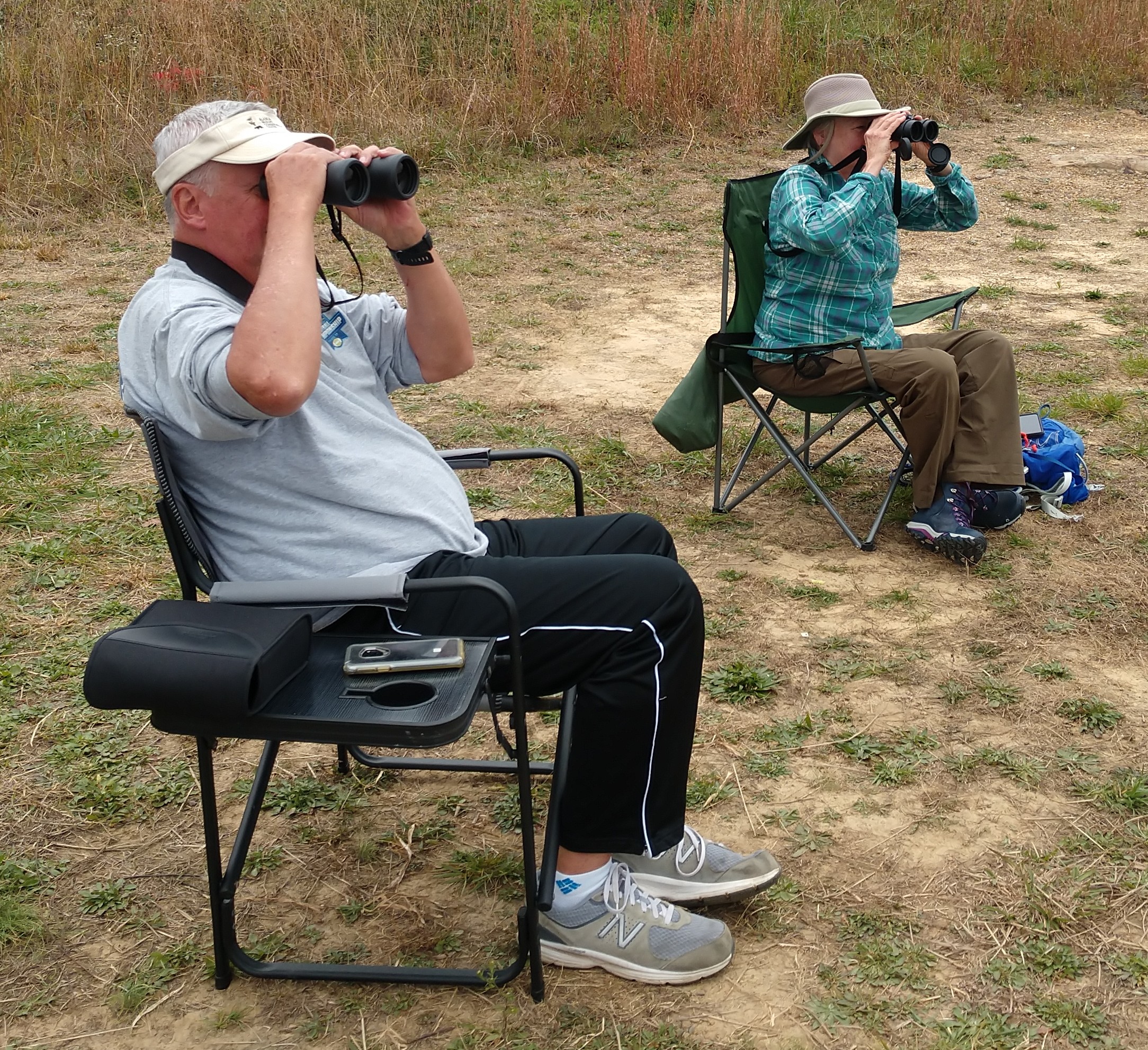 Two people seated outdoors, looking through binoculars