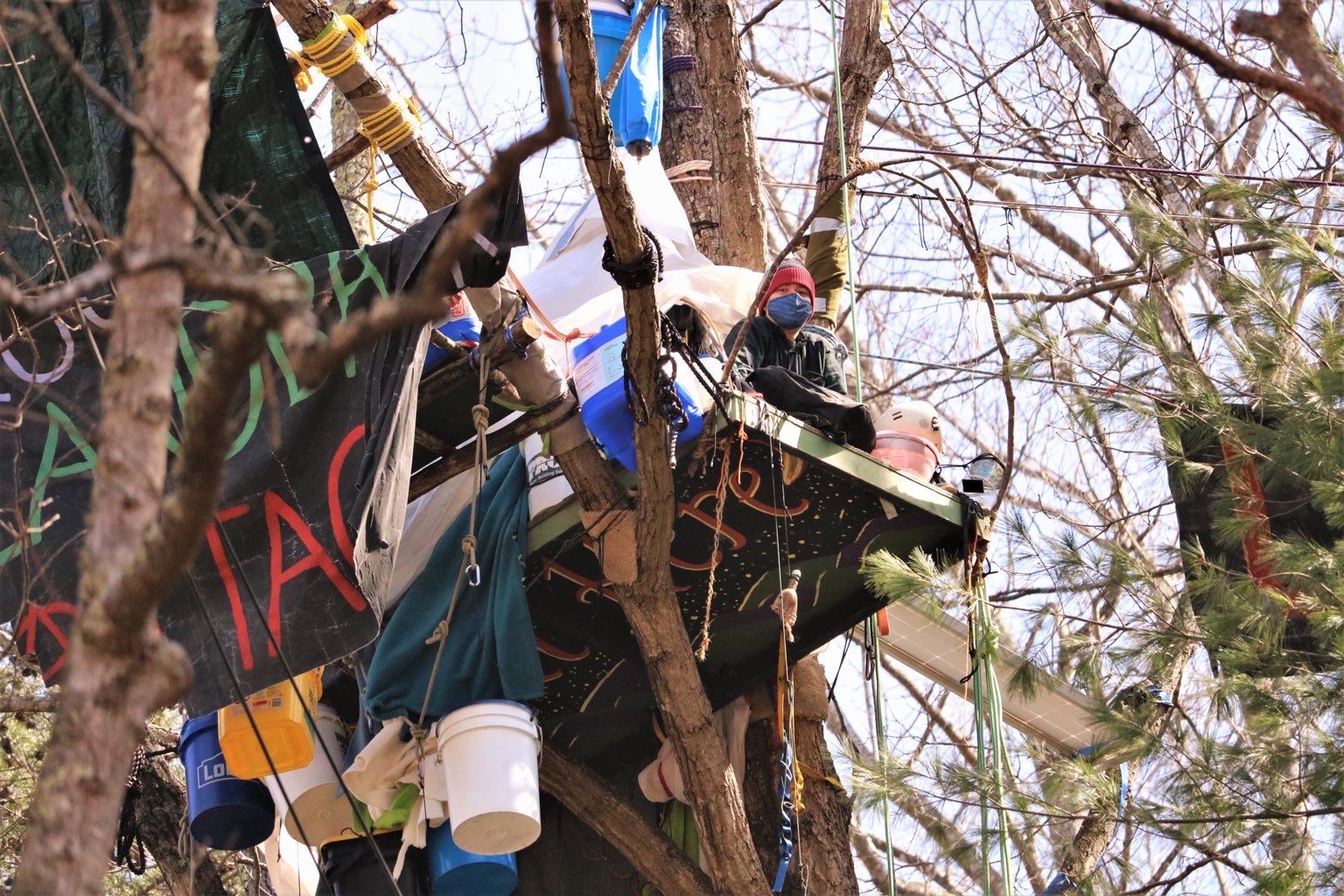 person sits on a platform in a tree that is attached to banners and buckets