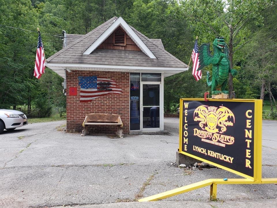 small brick building with welcome sign and American flags
