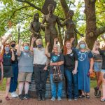 10 people raise their fists in front of a bronze statue