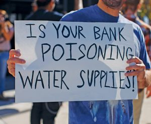 A demonstrator holds a sign during a Knoxville, Tenn., event that focused on the banks funding DAPL. Photo by  Lou Murrey 