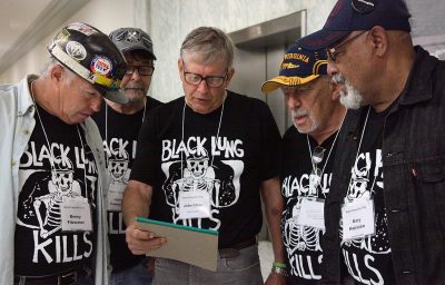 five miners wearing shirts that say Black Lung Kills gather around a notepad