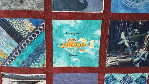 close-up of three quilt squares; one features different blue patterned cloth, another shows a fish with the words "Greenbrier River" and the third is abstract dark and white imagery