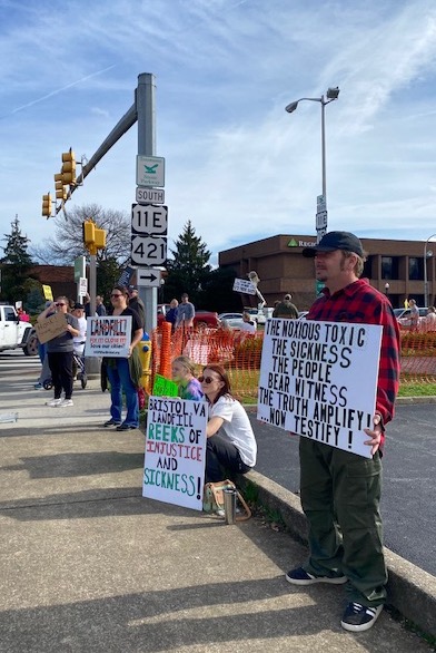 people hold homemade signs calling attention to health concerns and the terrible smell