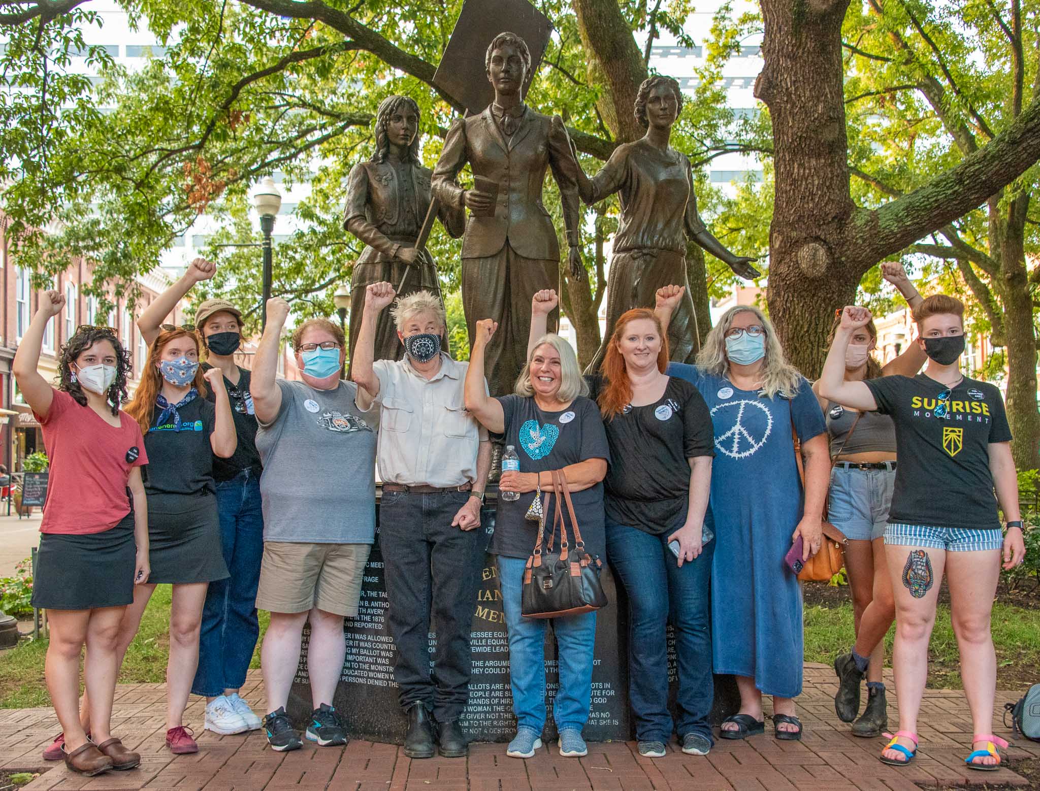10 people raise their fists in front of a bronze statue