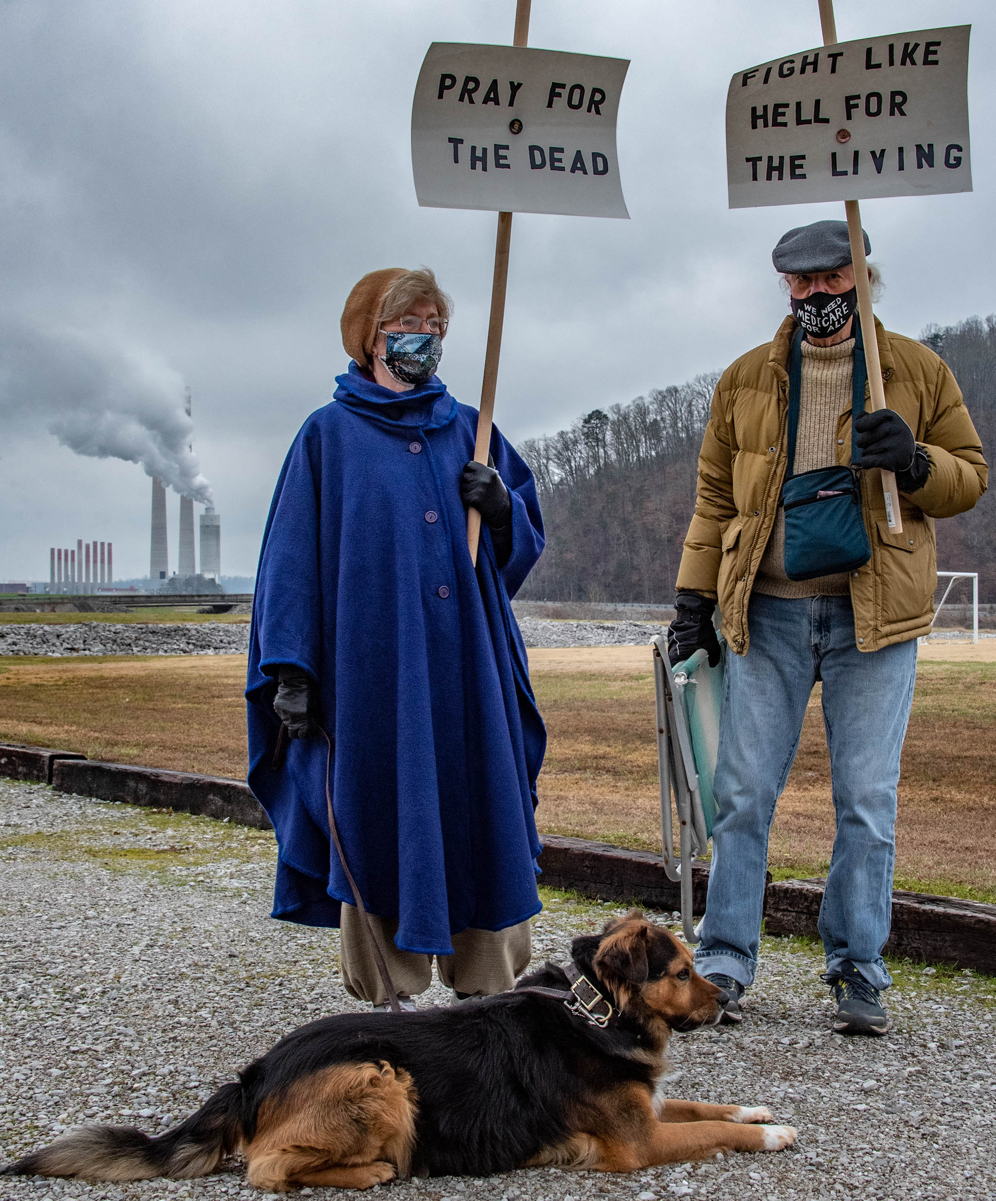 A man and woman hold signs that say "Pray for the dead" and "Fight like hell for the living" outside of the Kingston coal-fired power plant