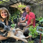 three smiling people and a dog in a greenhouse