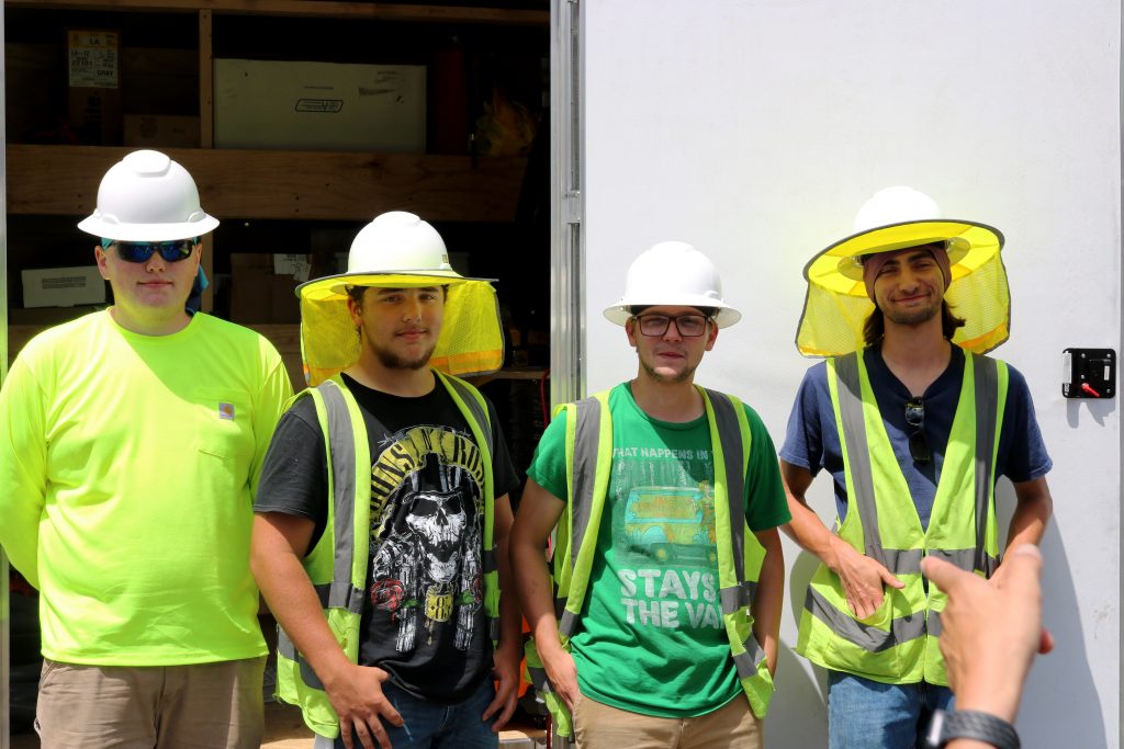Four apprentice installers stand outside in neon vests and construction hats.