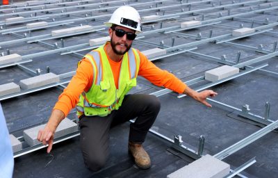 A project manager in a neon vest and construction hat kneels atop the roof of the St. Paul school..