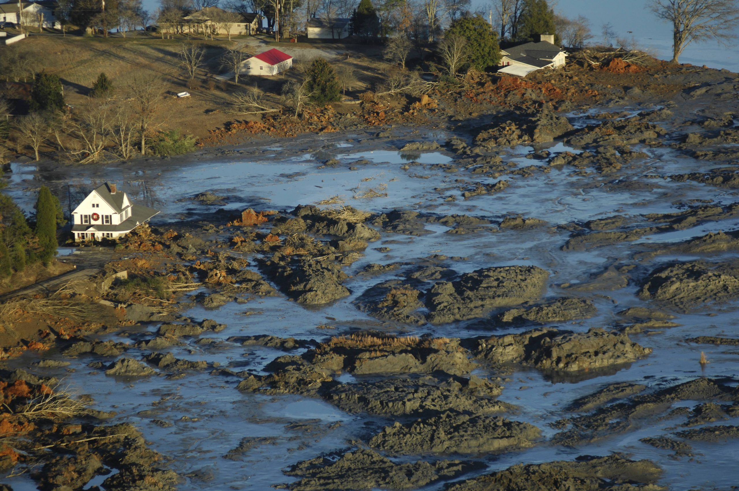 gray waste is piled high and surrounded by water near several homes