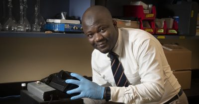 man in a tie and blue surgical glove holds a piece of research equipment