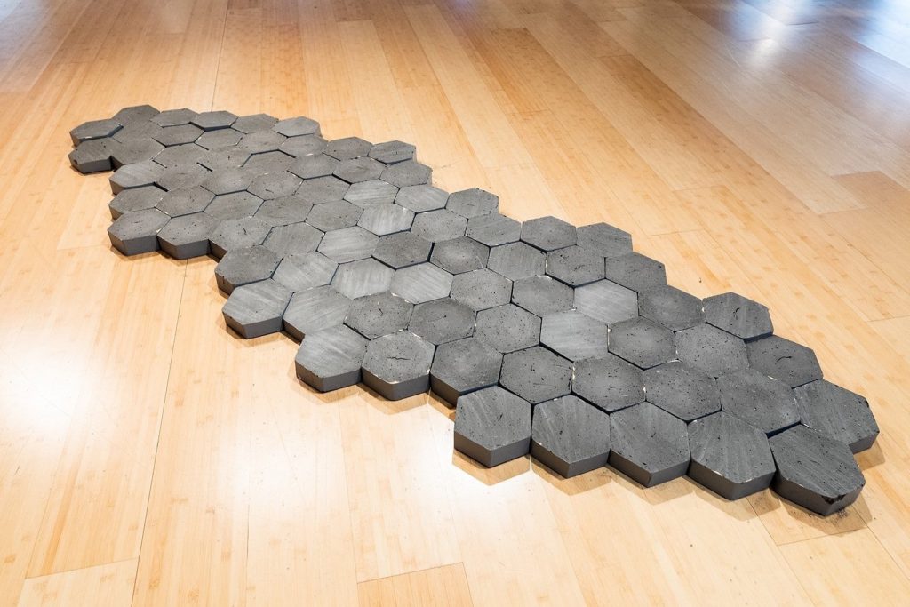 Grey hexagonal stones form a sandbar in an art gallery.
