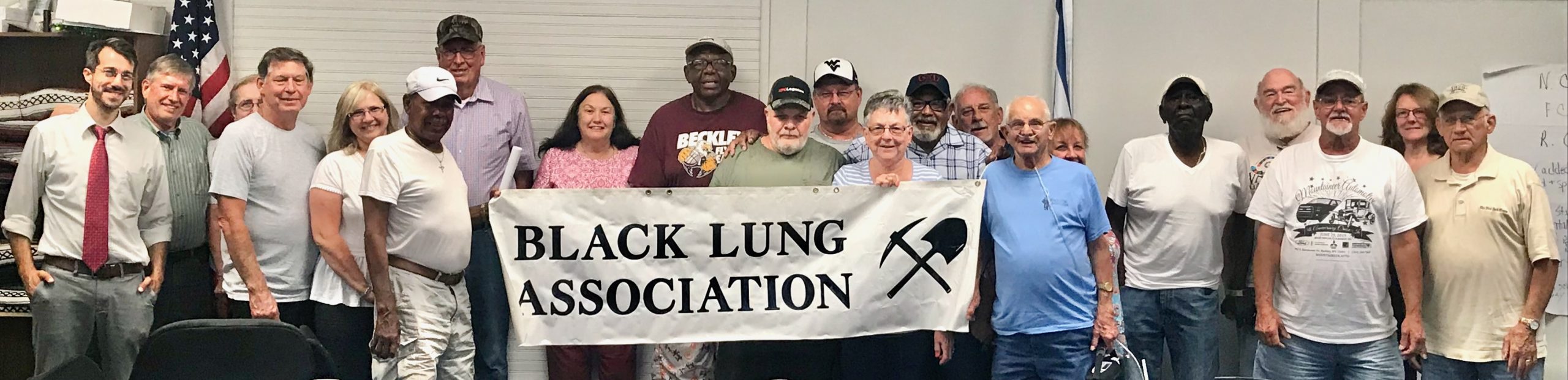 Men and women are gathered in a meeting room holding a sign that reads, "Fayette County Black Lung Association."