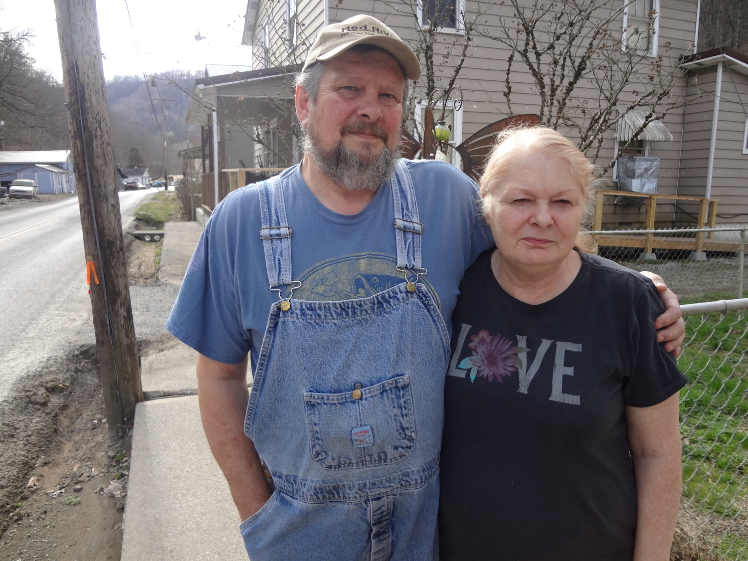 a man in overalls has his arm around a woman on the sidewalk