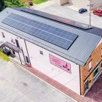 An aerial photo looks down on a white, rectangular building with solar panels on its rooftop. A pink sign on the side of the building bears the name Annie's Frugal Finery.