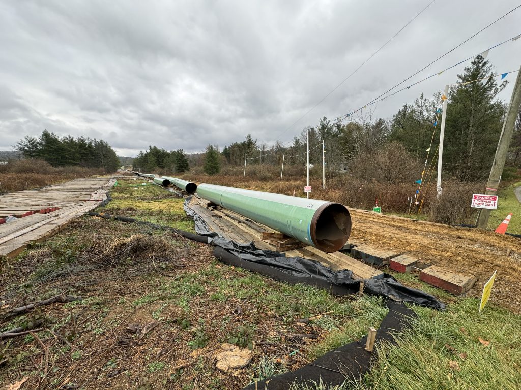 Sections of green pipe sit beside a temporary road made from timber mats in the right-of-way that cuts across a driveway.