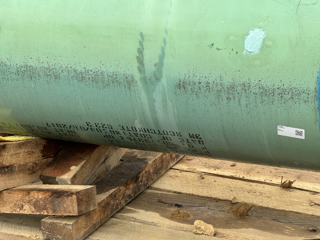 A dark splotch of fresh coating is visible on a large, green pipe that sits out in the elements.