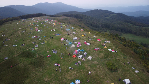 An aerial image shows dozens of colorful tents and litter on a mountain bald.
