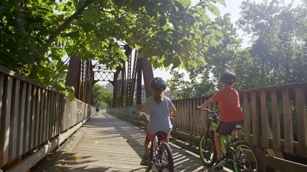 Children ride bikes over a wooden bridge.