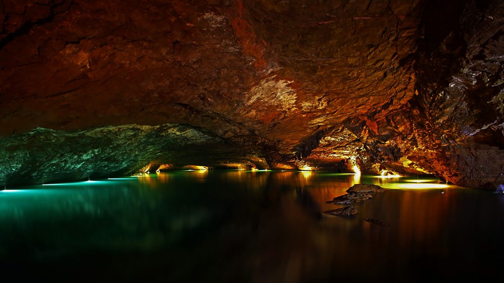 An underground lake and cavern are illuminated by colored lights.
