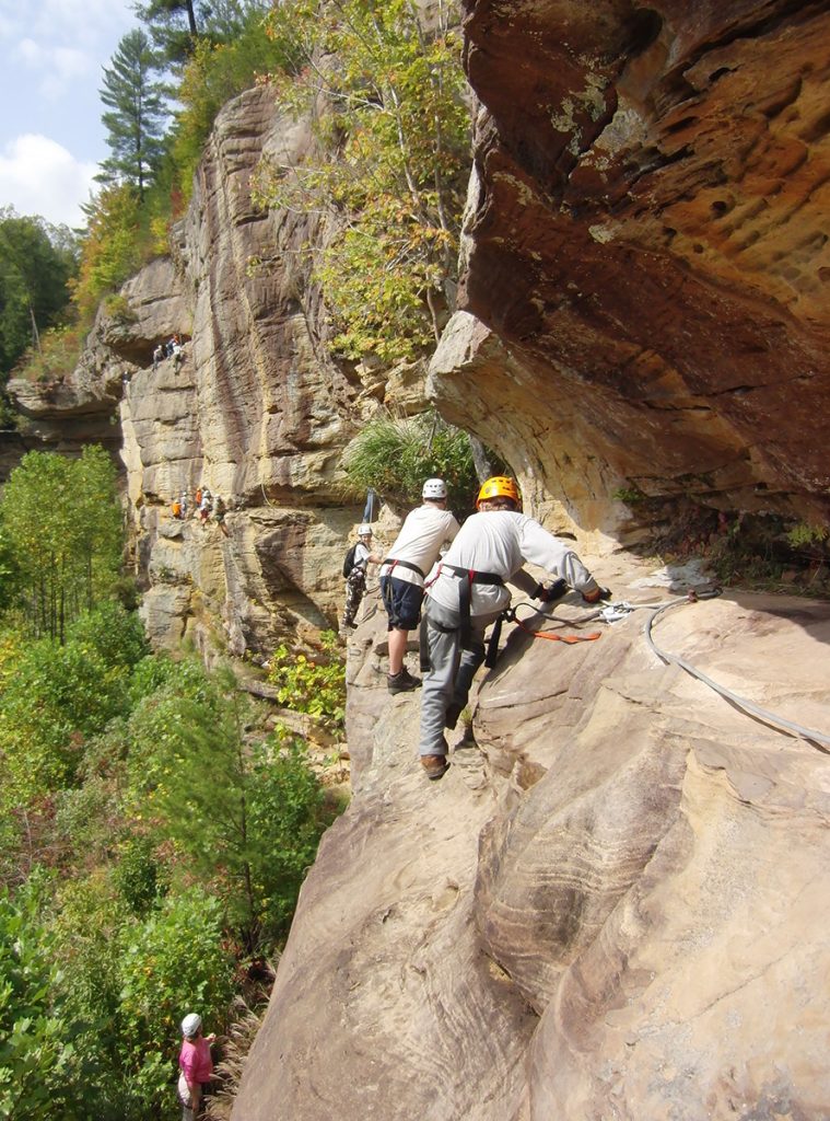 Climbers wearing harnesses and hardhats make their way along a rock wall.