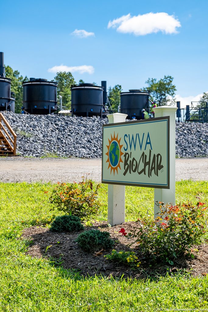 A brightly colored sign saying SWVA Biochar sits in the foreground with large kilns in the background.