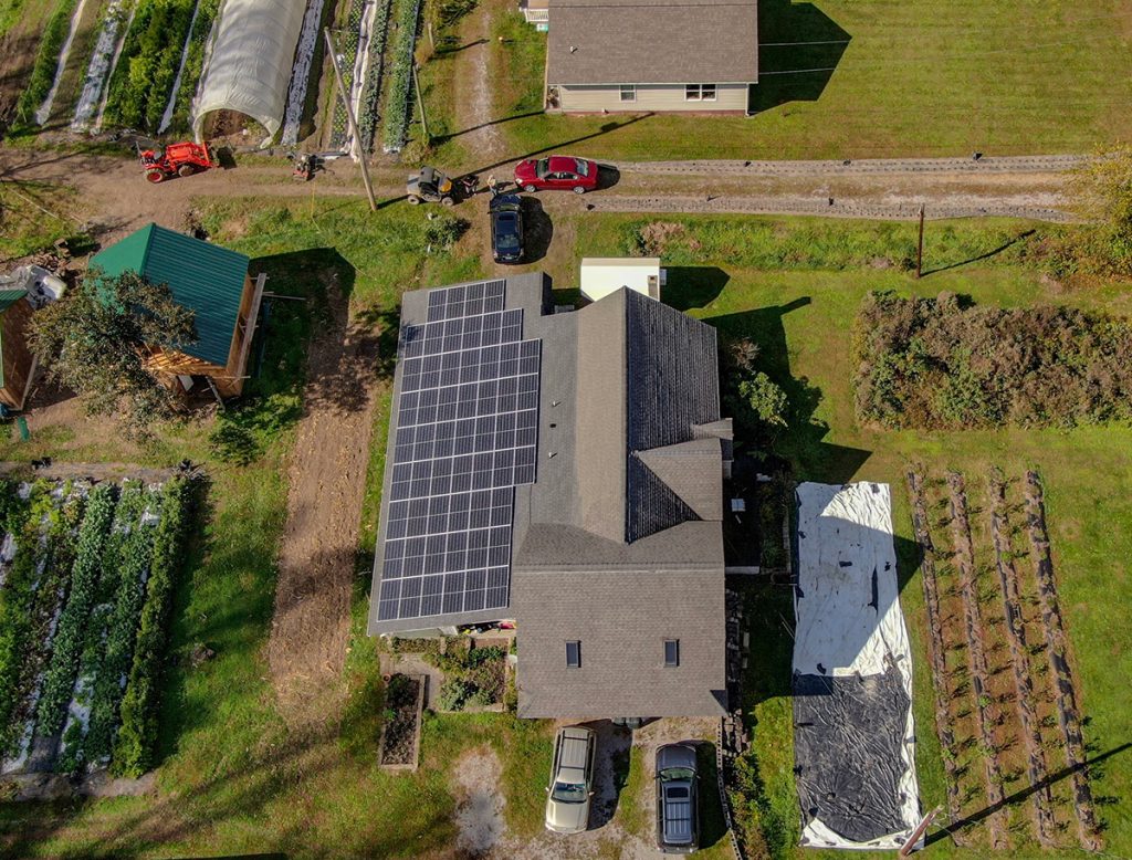 Solar panels fill a rooftop on a building located on a farm.