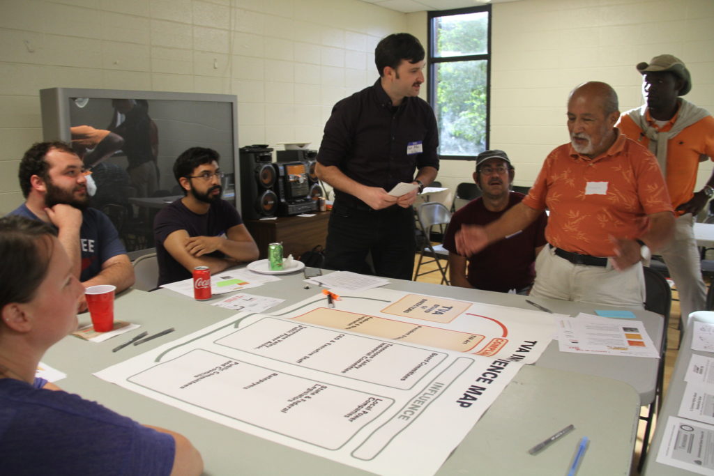 Participants gather around a table with large sheets of paper