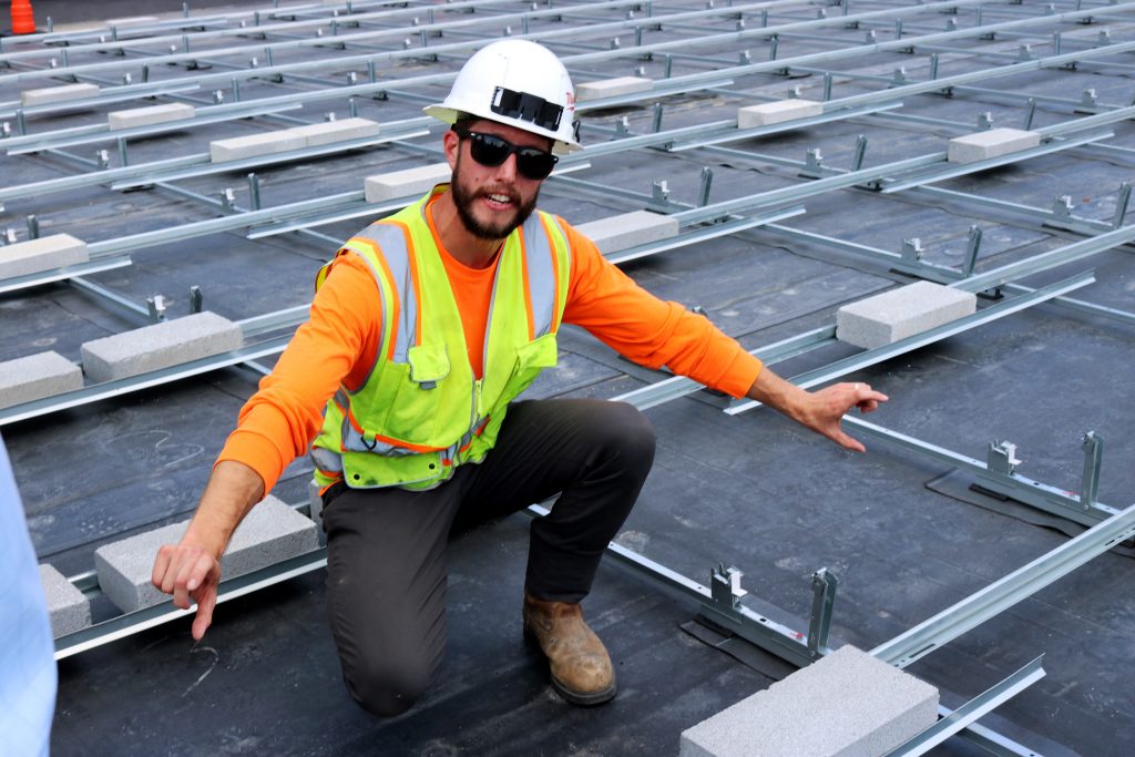 A project manager in a neon vest and construction hat kneels atop the roof of the St. Paul school..