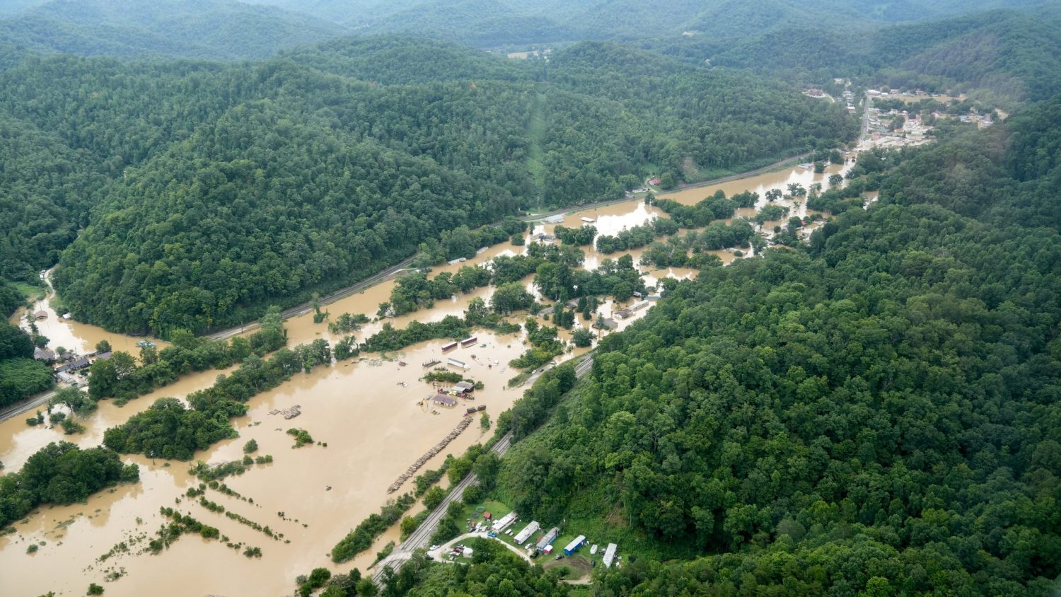 An aerial photo shows muddy water overflowing the banks of a river and flooding a town in a Kentucky valley.