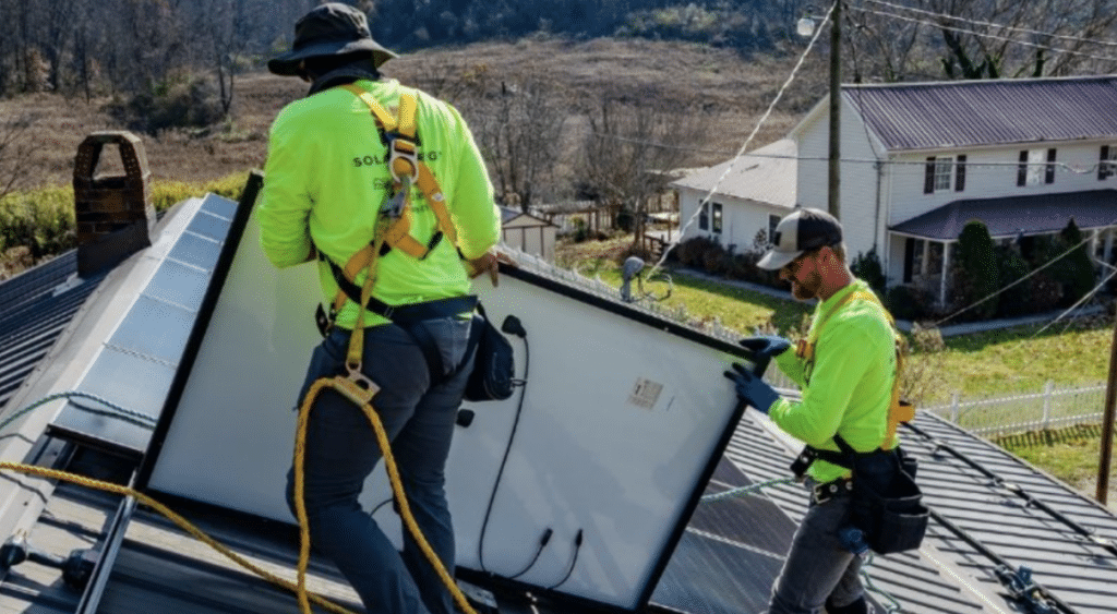 Two workers install solar panels on a rooftop array.