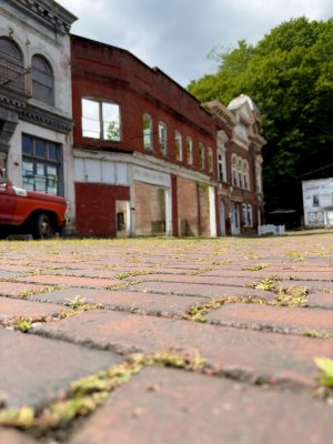 The camera, at ground level, looks across weathered, moss-covered bricks with that appear to be early 20th-century architecture in the background.