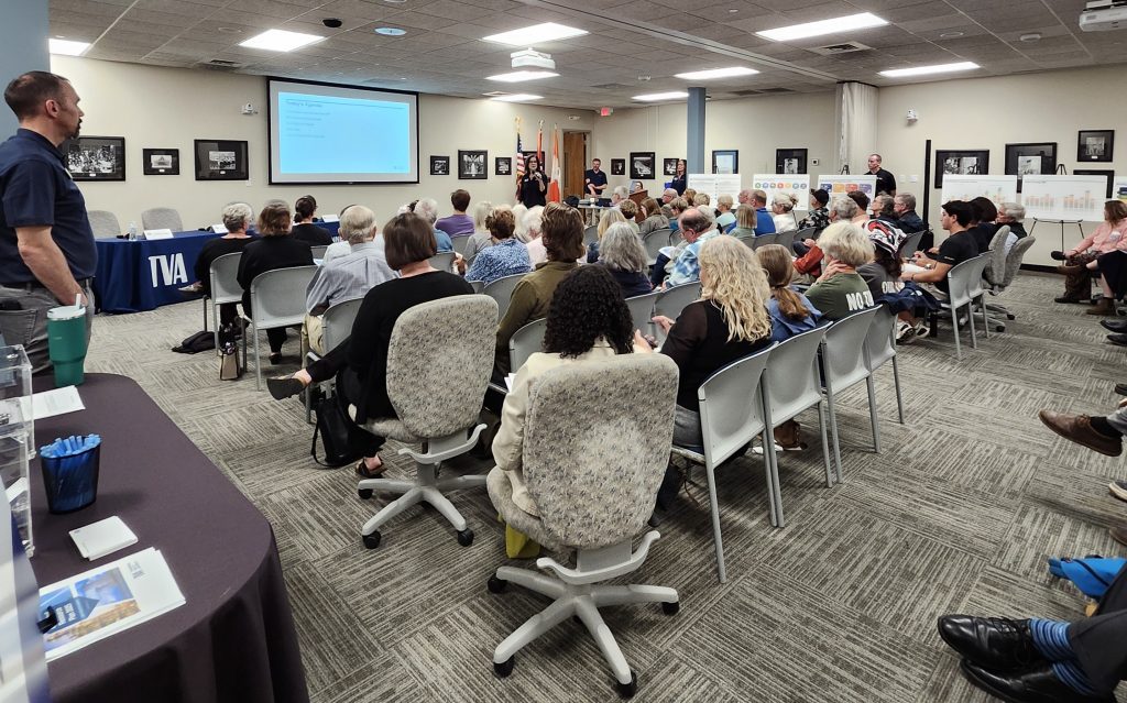 several dozen attendees sit an listen to a speaker from TVA, various charts are displayed