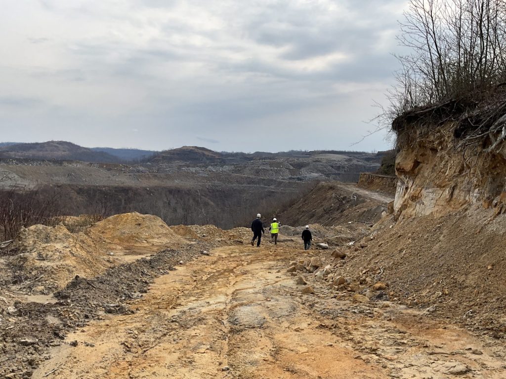 Three people walk down a rough mine road in the middle of a large surface mine, surrounded by rock and dirt