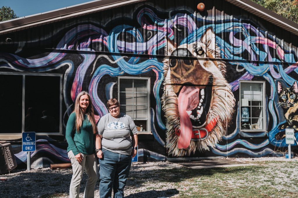 Photo of two people in front of an animal shelter with a colorful mural of a dog. Photo by Michael Chassereau from Forever and Always Photography.