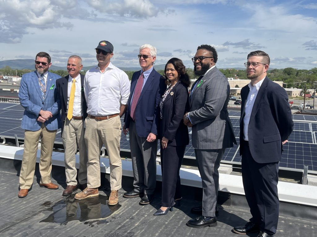 Group of people smile for poised photo in front of 300 solar panels atop the three-story William B. Robertson Administration Building in downtown Roanoke.