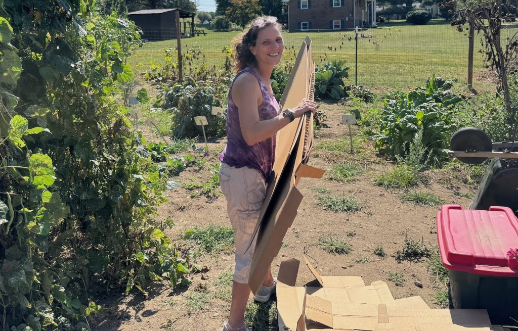 Women in a garden holding cardboard. Woman is Crystal Mello, who works in the Eastmont Community Garden she helped establish. Photo by Dan Radmacher