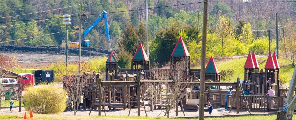 Children play at a playground with a coal ash pile behind it