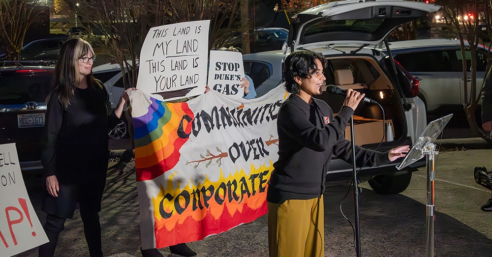 Person speaks out at SSEP protest with protest banners behind them