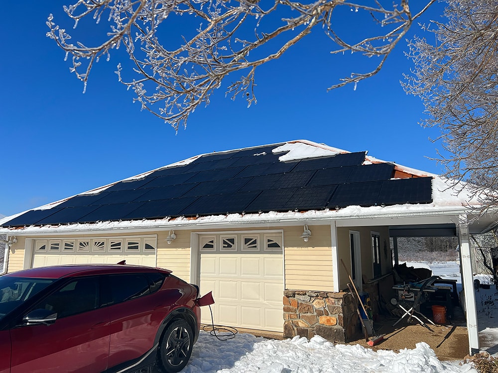 A home with solar panels covered in snow with an EV parked outside and a blue sky 