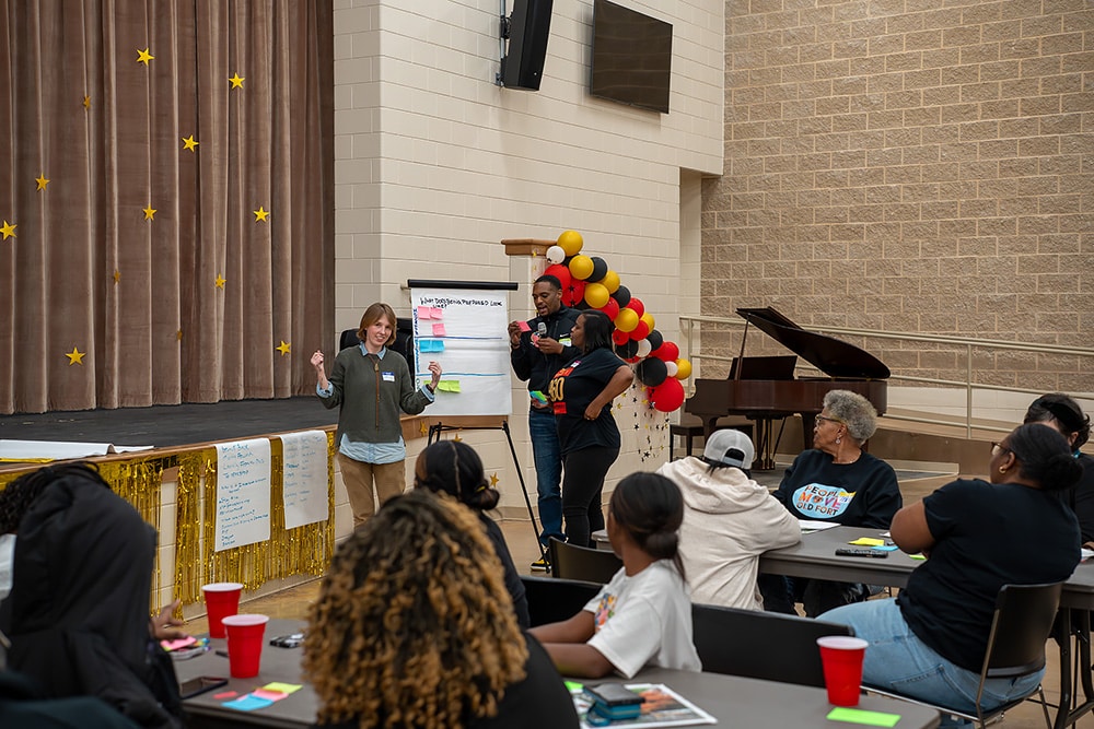 People talk in front of a crowd in a school gym