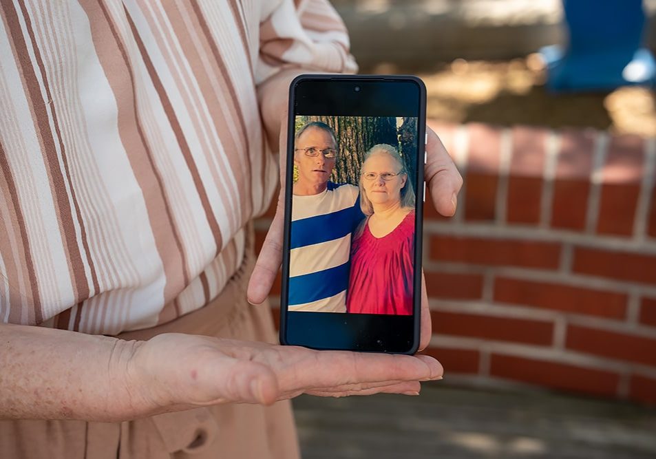A woman holds a photo of her parents on her phone